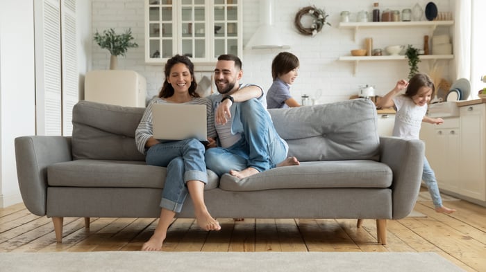 Husband & Wife sitting in living room, while kids play.